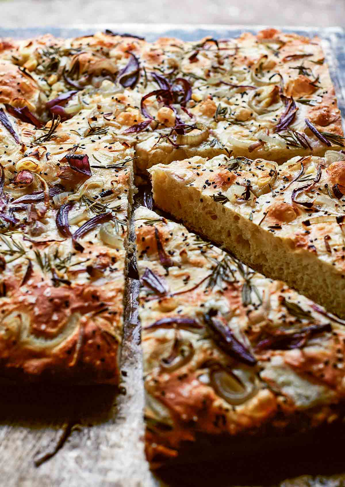 A baked loaf of focaccia with red onion and rosemary with two wedges cut from it.