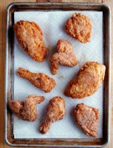 Seven pieces of gluten-free fried chicken on a paper towel-lined rimmed baking sheet.