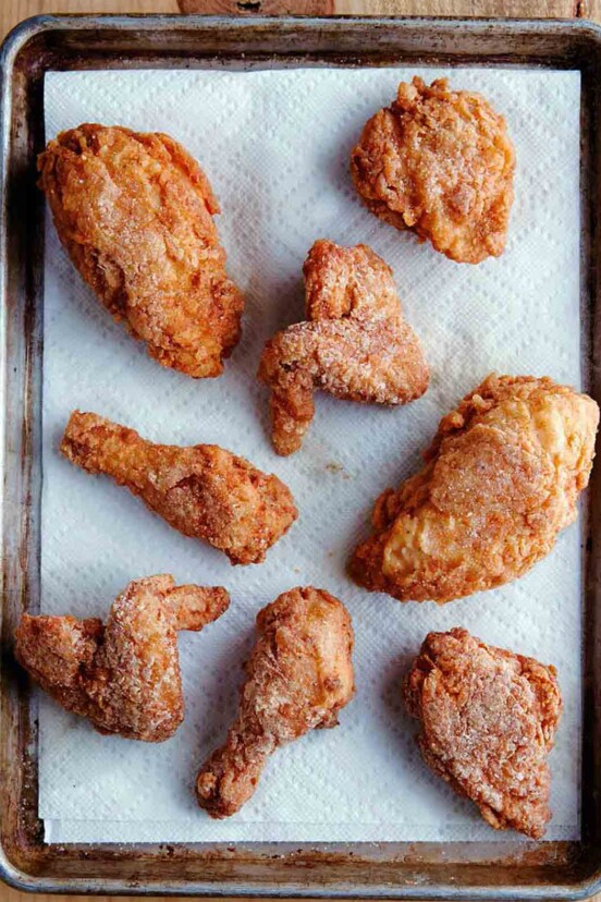 Seven pieces of gluten-free fried chicken on a paper towel-lined rimmed baking sheet.