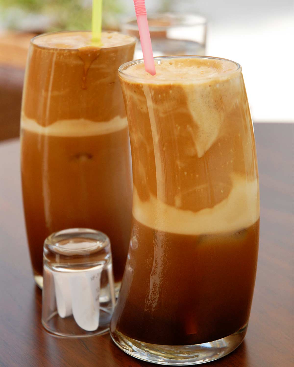 Two tall glasses filled with Greek-style frappe, with colorful straws standing up in them.