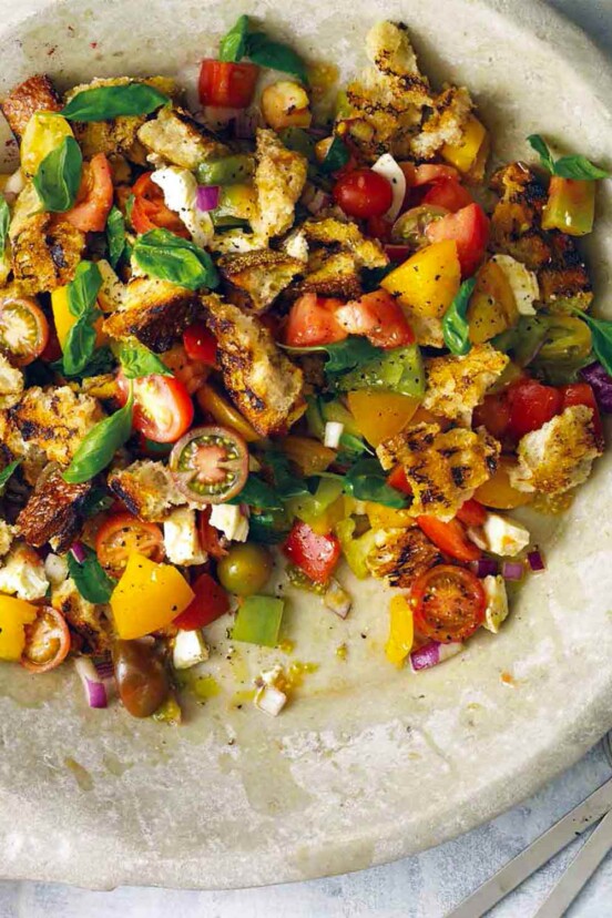 A large bowl filled with grilled panzanella, with cherry tomatoes, torn bread, and basil leaves.