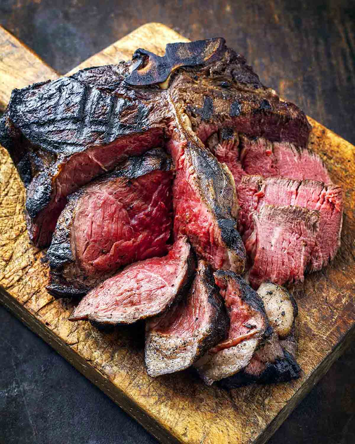 A partially sliced grilled porterhouse steak on a wooden cutting board.