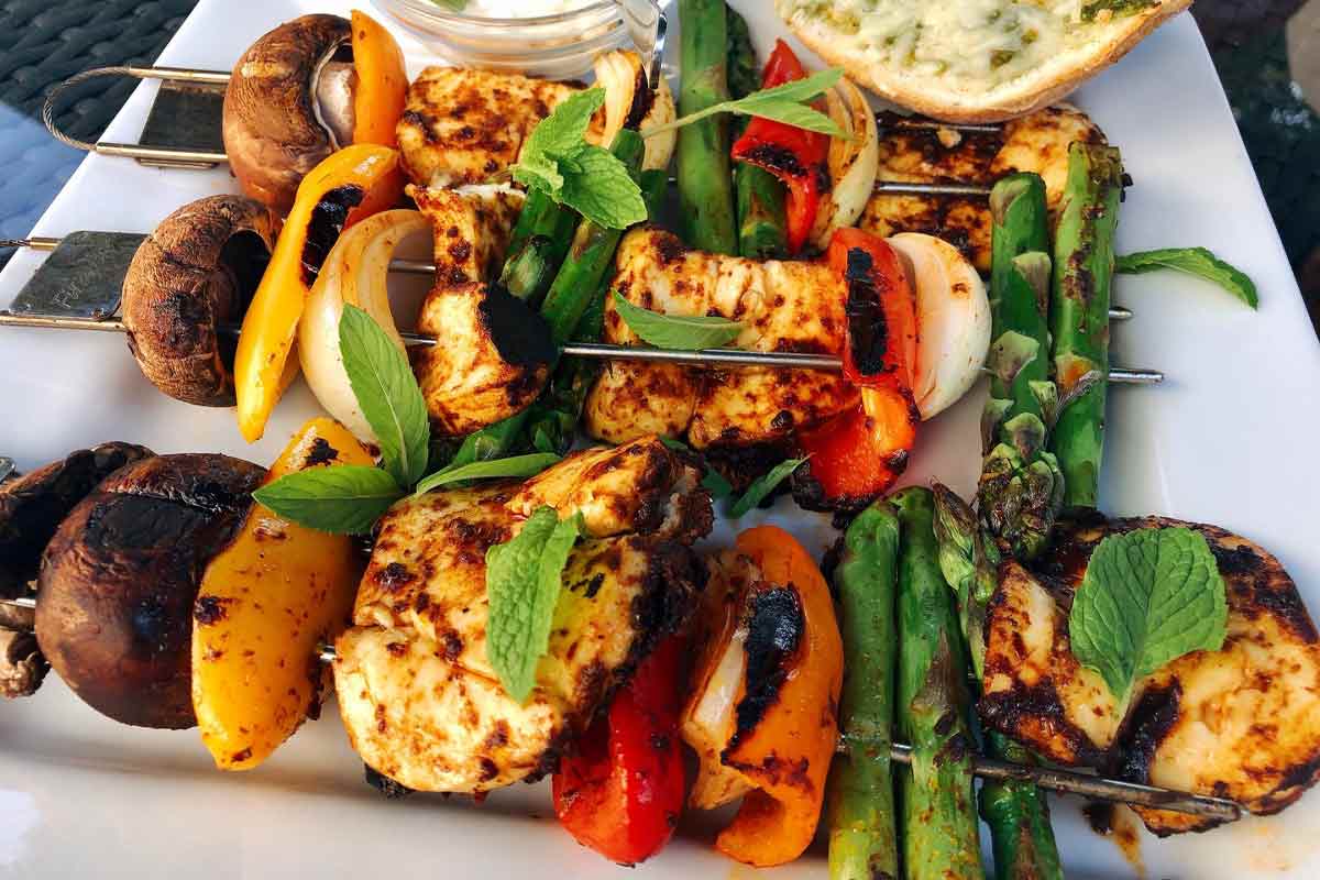 Three harissa vegetable skewers with halloumi on a white plate.