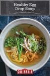 A bowl of healthy egg drop soup with shredded chicken, green onions, broccoli rabe, noodles, and sprouts