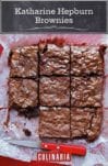 A slab of Katharine Hepburn brownies cut into 9 pieces, on parchment paper, with a knife nearby