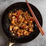 A wok filled with kung pao chicken with two chopsticks on the edge