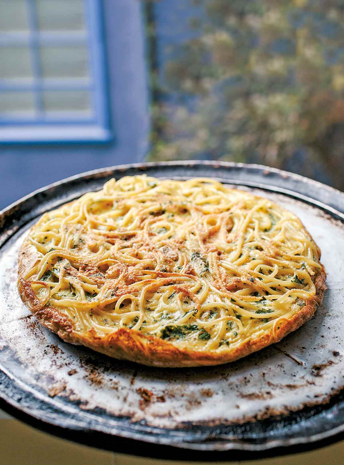 A cooked leftover pasta frittata on a round metal pan.
