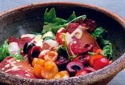 A ceramic bowl filled with mixed green salad with Prosciutto and cherries and drizzled with creamy Dijon dressing.