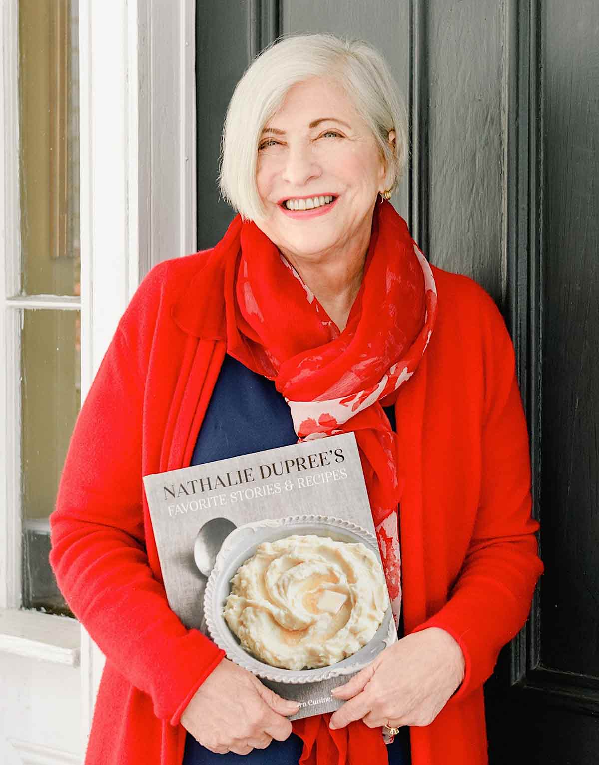 Nathalie Dupree in red sweater holding her cookbook.