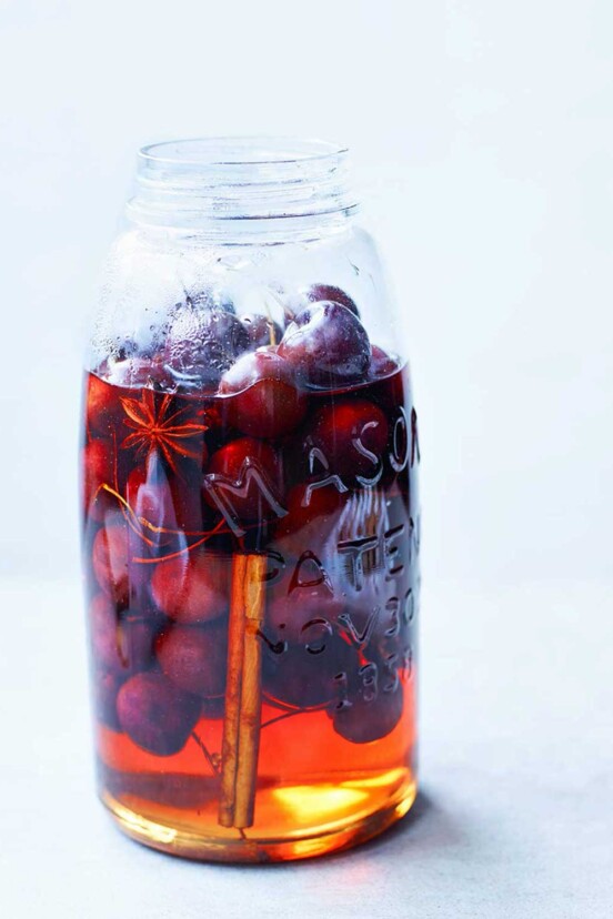 A mason jar mostly filled with pickled cherries, pickling liquid, star anise, and a cinnamon stick.
