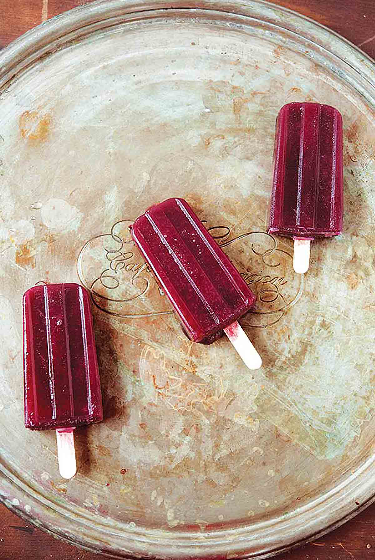 Three red wine popsicles on a silver tray.