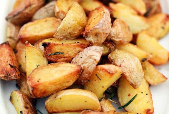 A platter of quartered roasted potatoes on the grill, seasoned with pepper and rosemary.