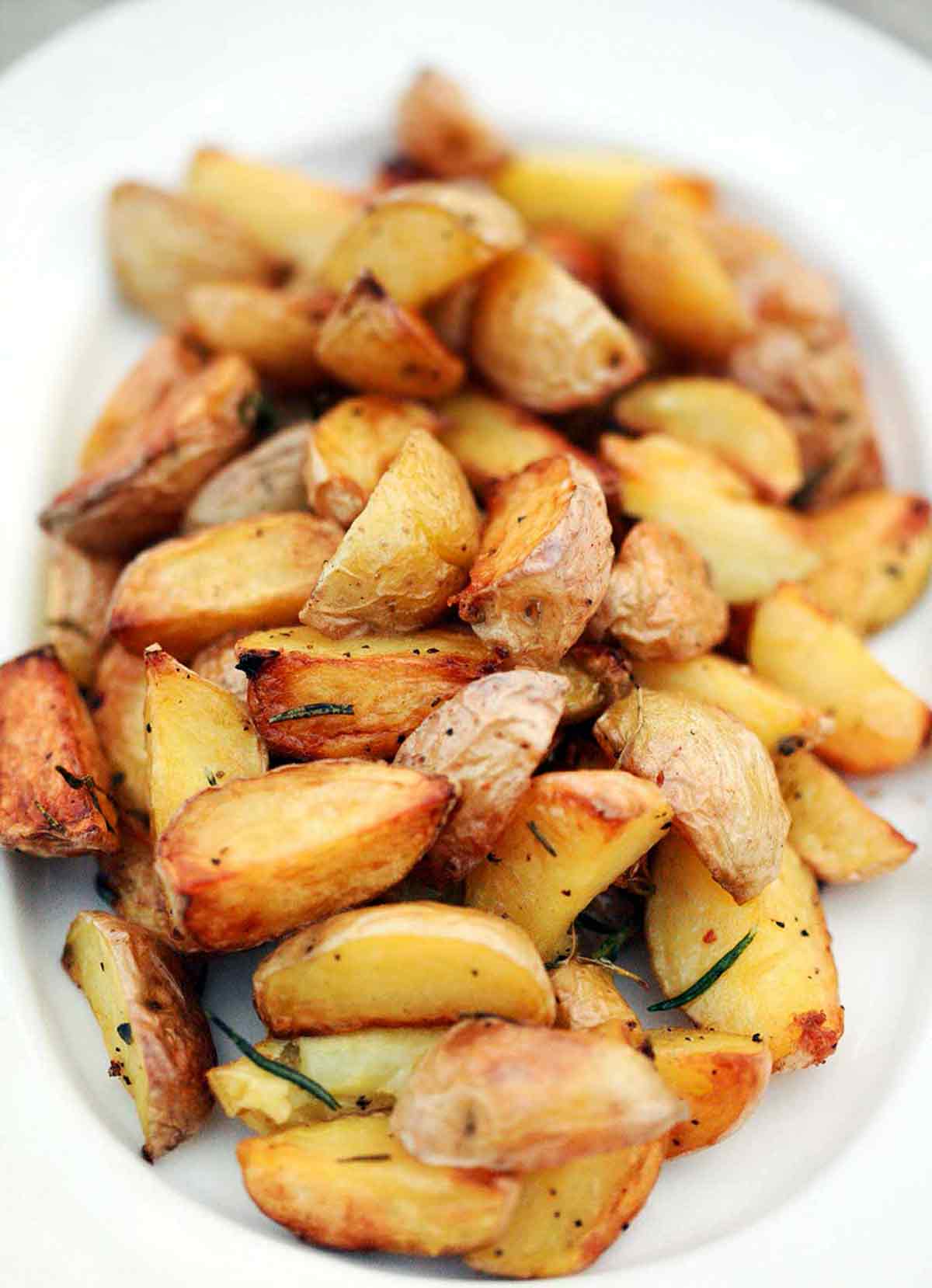 A platter of quartered roasted potatoes on the grill, seasoned with pepper and rosemary.