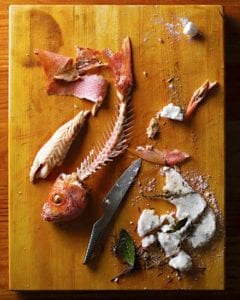 A salt-baked red snapper with all the flesh removed from the bones and a broken salt crust and knife beside the fish skeleton.
