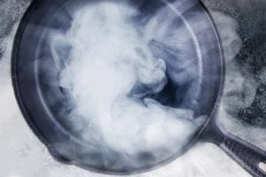 A cast-iron skillet with smoke billowing from an oil that has reached its smoke point.