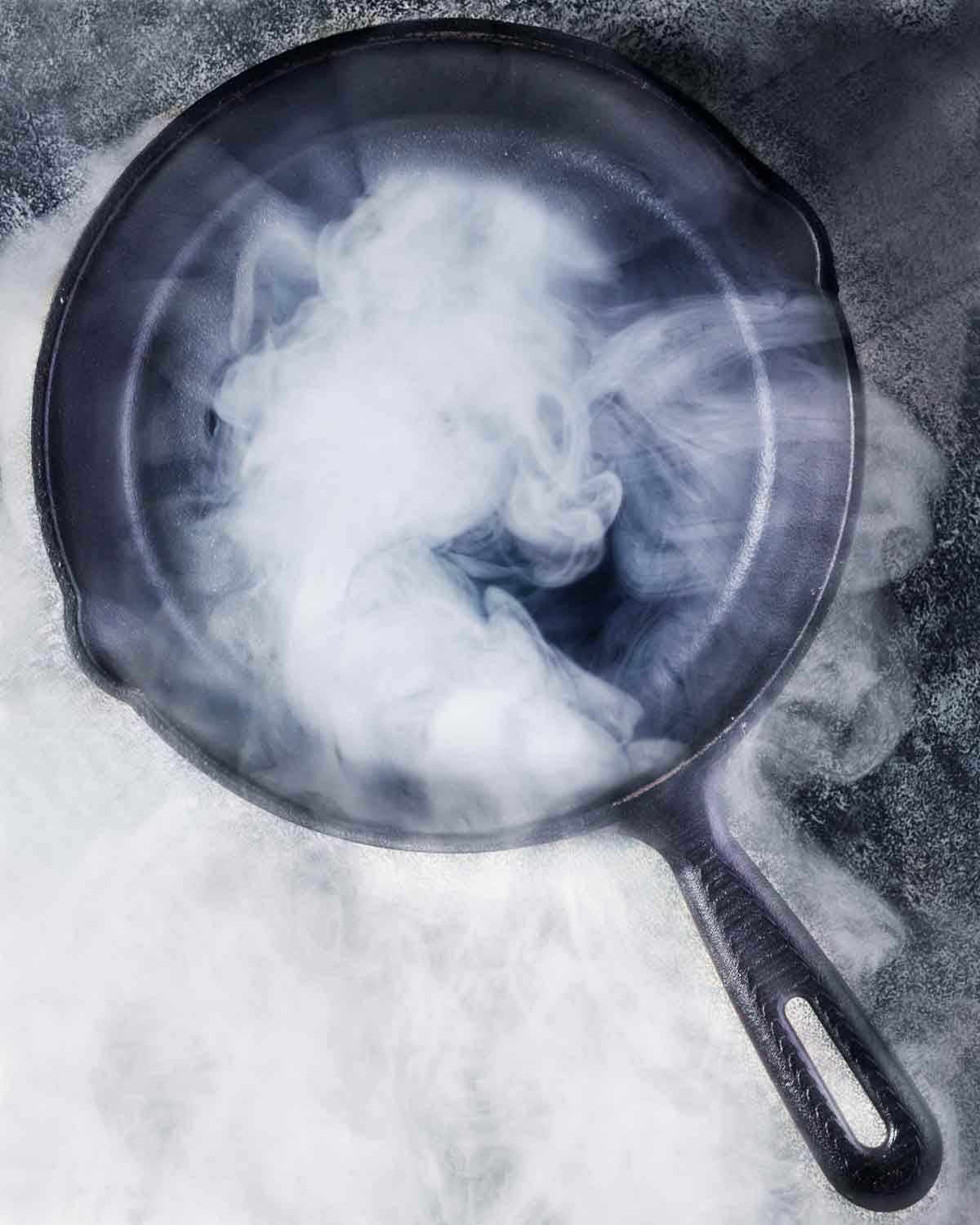 A cast-iron skillet with smoke billowing from an oil that has reached its smoke point.