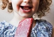 A little girl eating a strawberry ice pop.