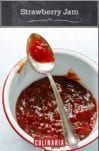 An enamel-coated pot filled with strawberry jam and a spoon resting on top.