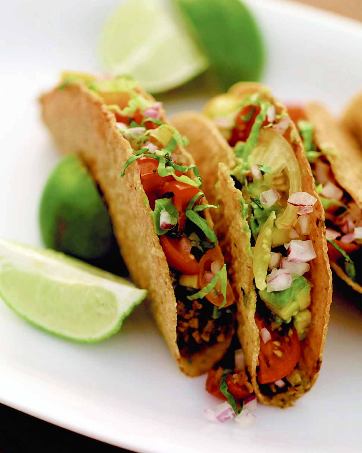 Tre söta och kryddiga tacos på en vit tallrik med limeklyftor bredvid.