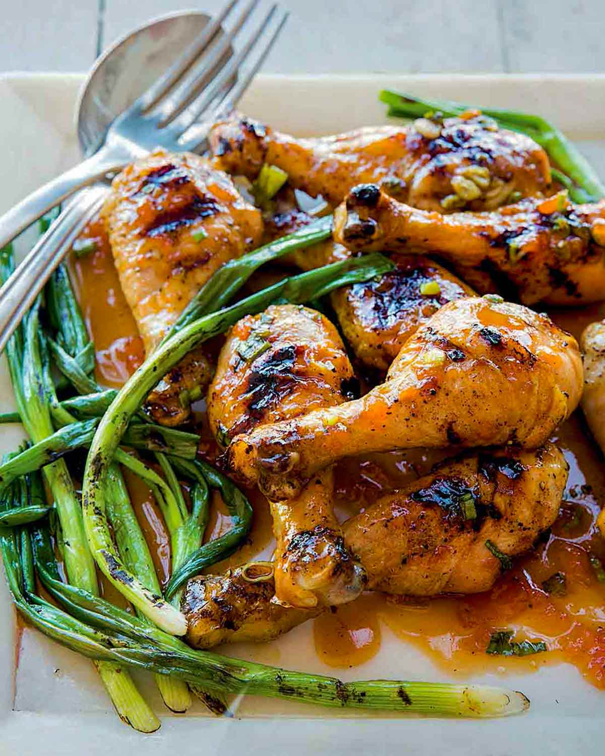 Square plate of a pile of grilled sweet and sticky sriracha drumsticks and grilled scallions