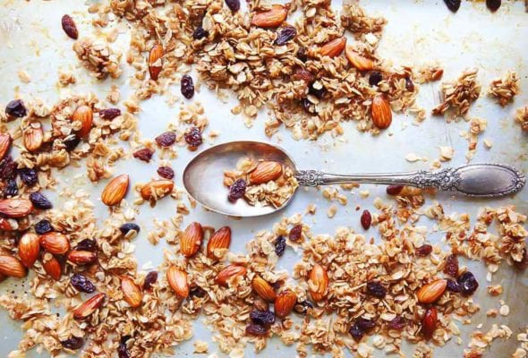 Almond and coconut granola scattered on a baking sheet with a spoon resting in the center.