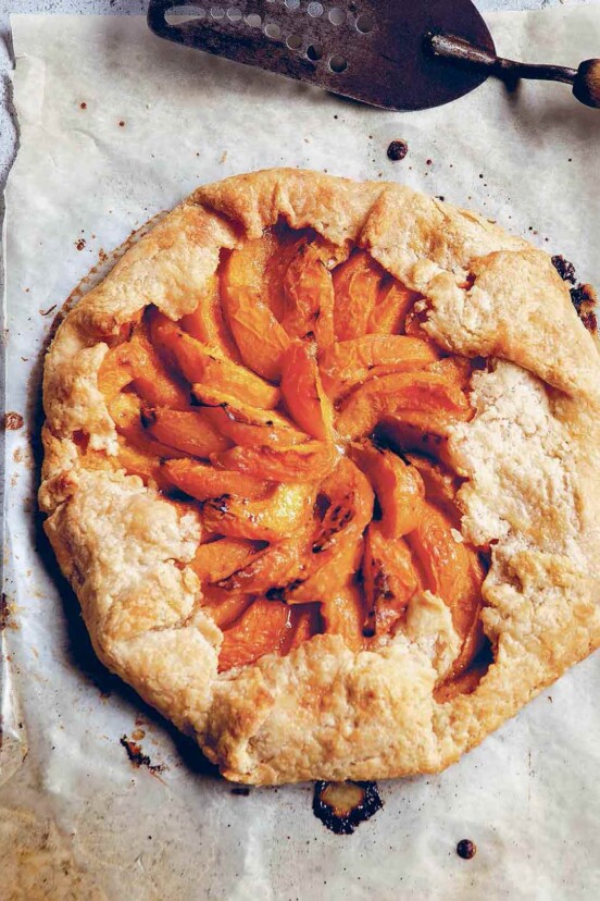 A cooked apricot galette on a piece of parchment paper with a metal spatula beside it.