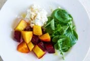 A white plate topped with beet salad with goat cheese and honey and watercress leaves.