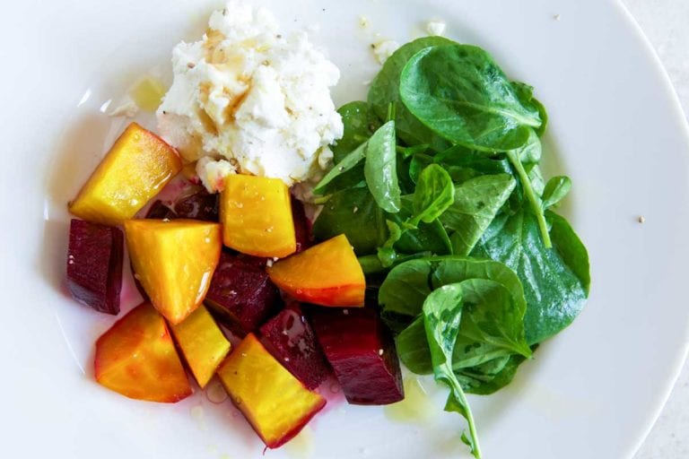 A white plate topped with beet salad with goat cheese and honey and watercress leaves.