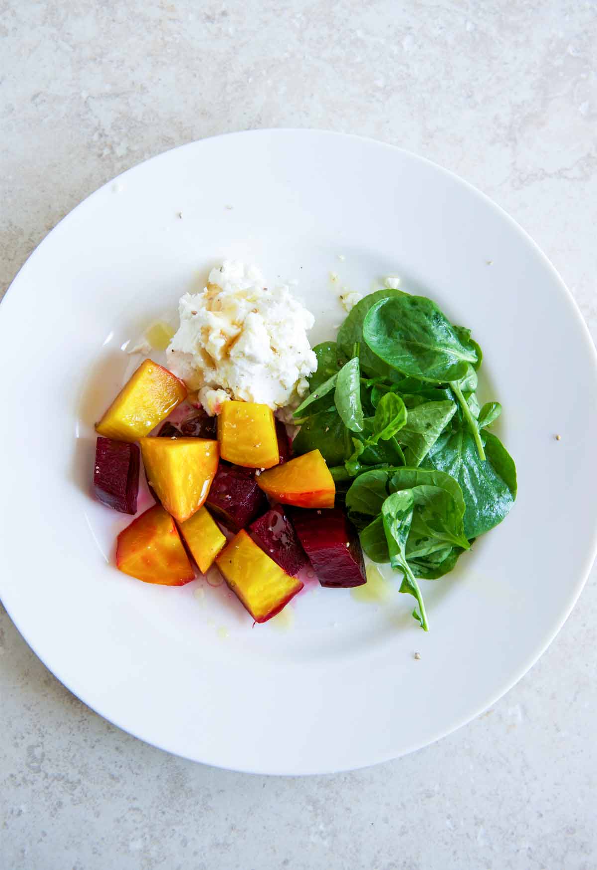 A white plate topped with beet salad with goat cheese and honey and watercress leaves.