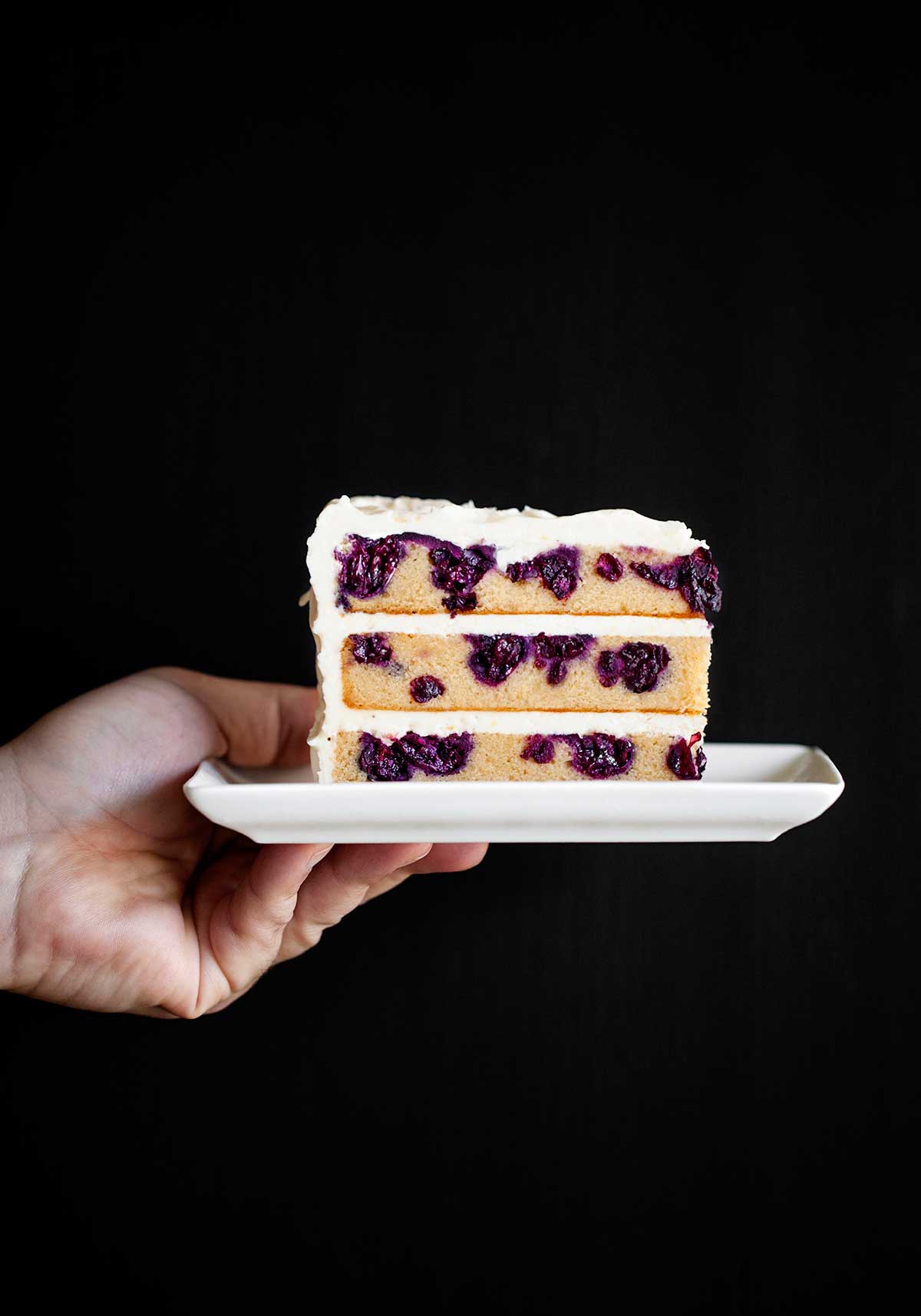 A white plate with a slice of blueberry-lemon layer cake