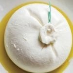 A ball of burrata for burrata with grilled bread sitting in a few tablespoons of oil in a white bowl.
