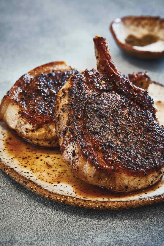 Two bone-in grilled Cambodian pork chops on a plate.