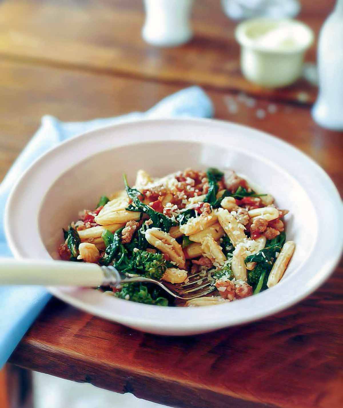 Bowl of cvatelli with turkey sausage, tomato, and broccoli rabe on a table, with a spoon