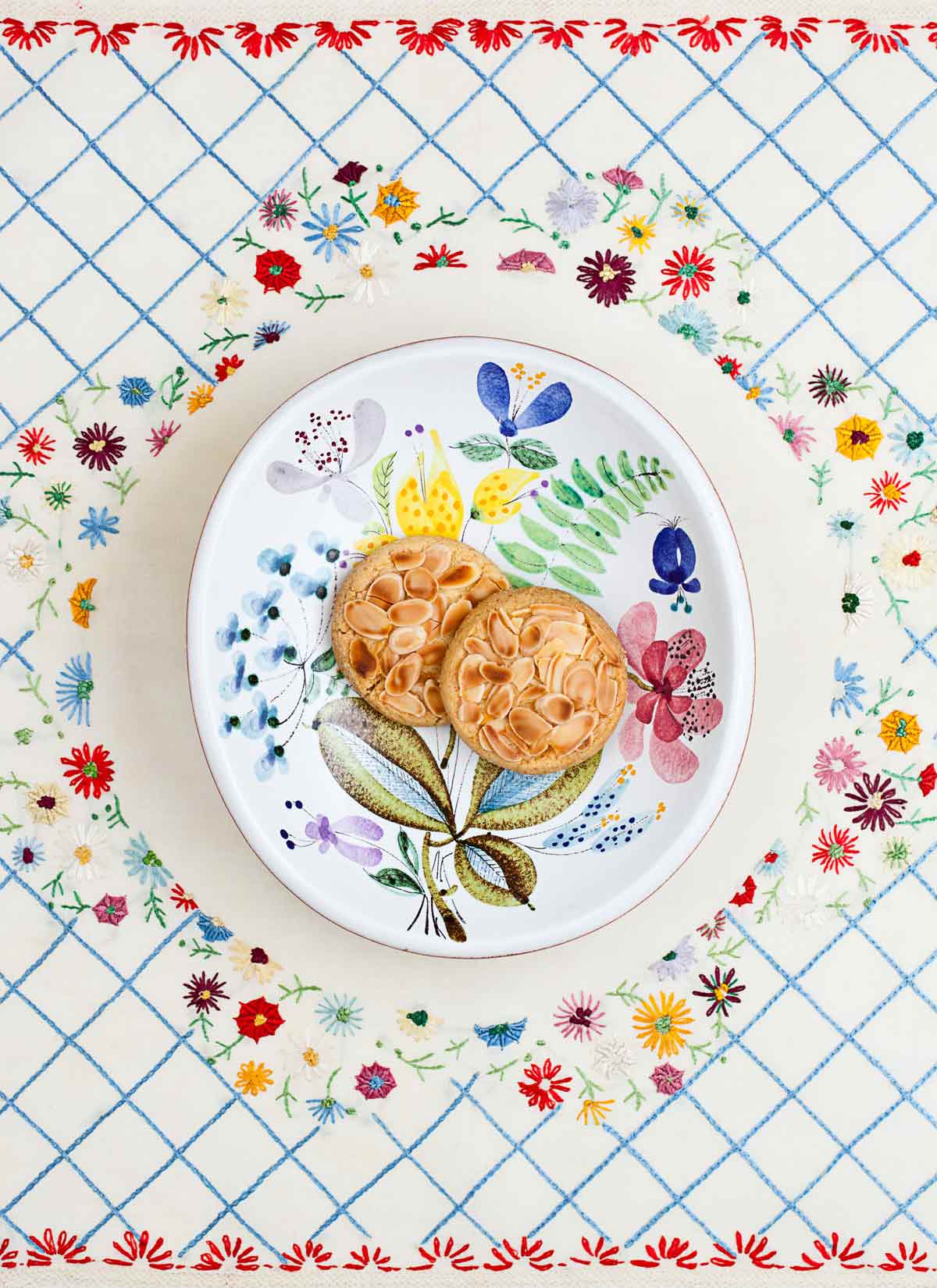 Two almond-topped cookies made by Cenk Sönmezsoy on a decorative plate and cloth.