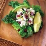 A serving of chicken avocado cranberry salad on a square wooden plate.