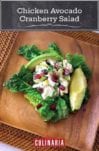 A serving of chicken avocado cranberry salad on a square wooden plate.