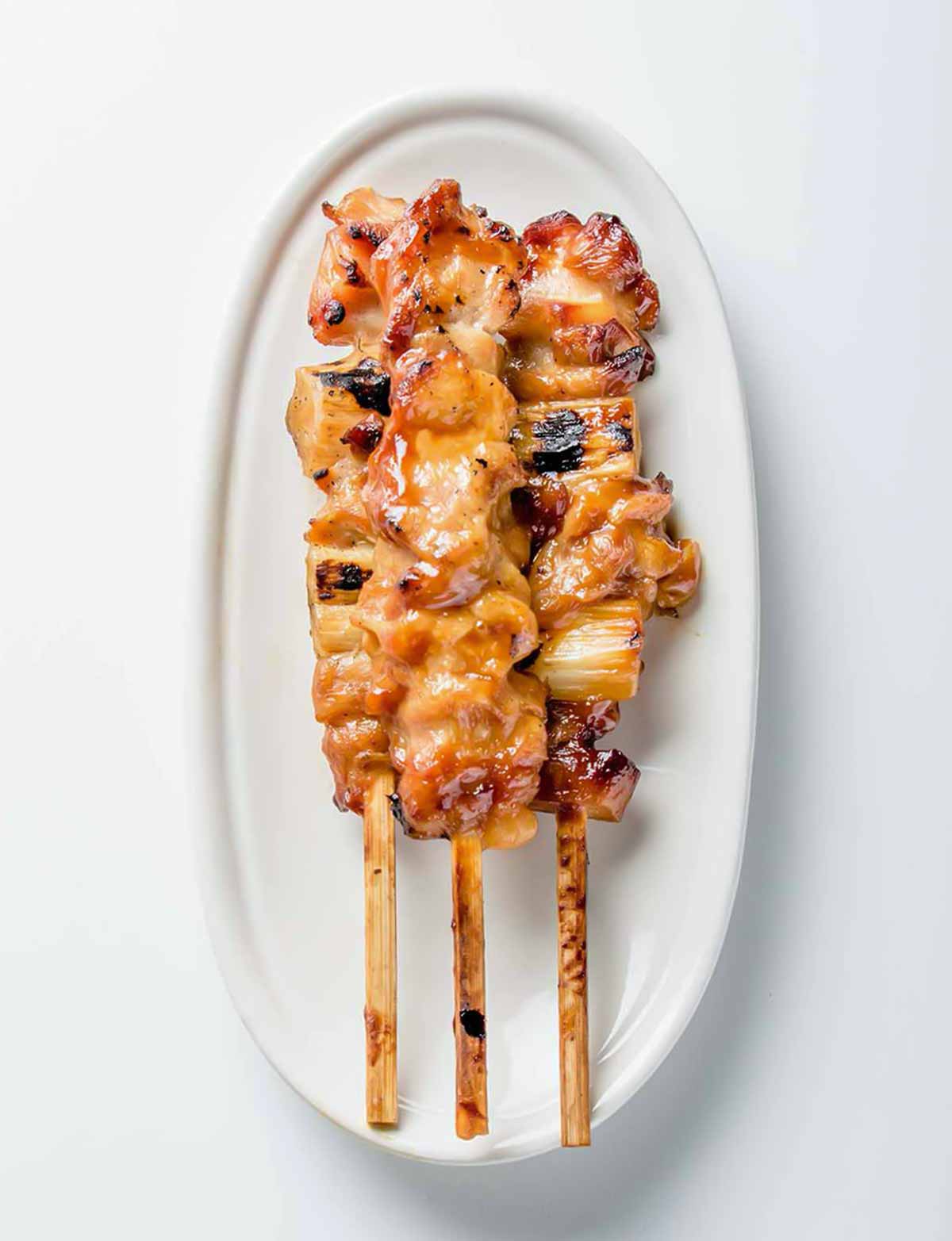 A white oval serving platter topped with three skewers of chicken yakitori with honey sauce.