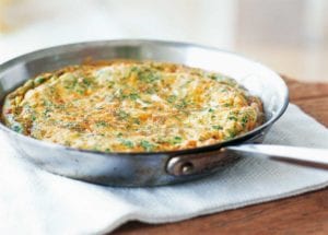 A frittata with leeks and herbs in a metal skillet on a white linen mat.