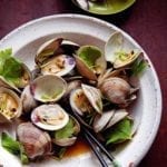 Bowl of grilled littleneck clams with soy sauce, cilantro leaves, and chopsticks