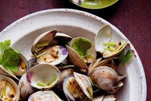 Bowl of grilled littleneck clams with soy sauce, cilantro leaves, and chopsticks