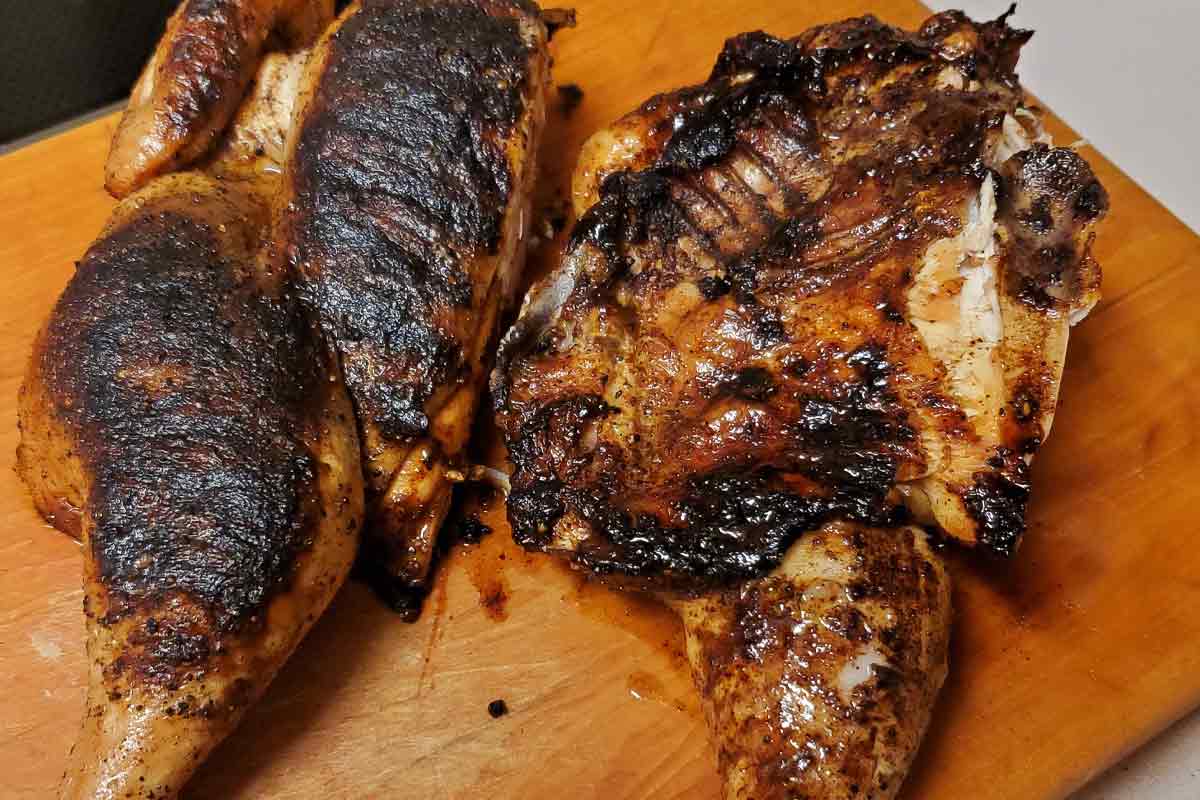 A grilled roasted chicken on a wooden cutting board.