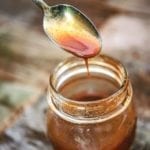 A half-full jar of honey barbecue sauce with a spoon dripping excess sauce back into the jar.