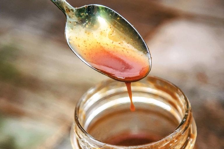 A half-full jar of honey barbecue sauce with a spoon dripping excess sauce back into the jar.