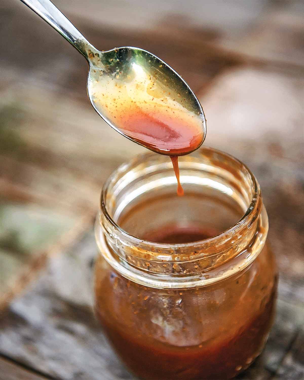 A half-full jar of honey barbecue sauce with a spoon dripping excess sauce back into the jar.