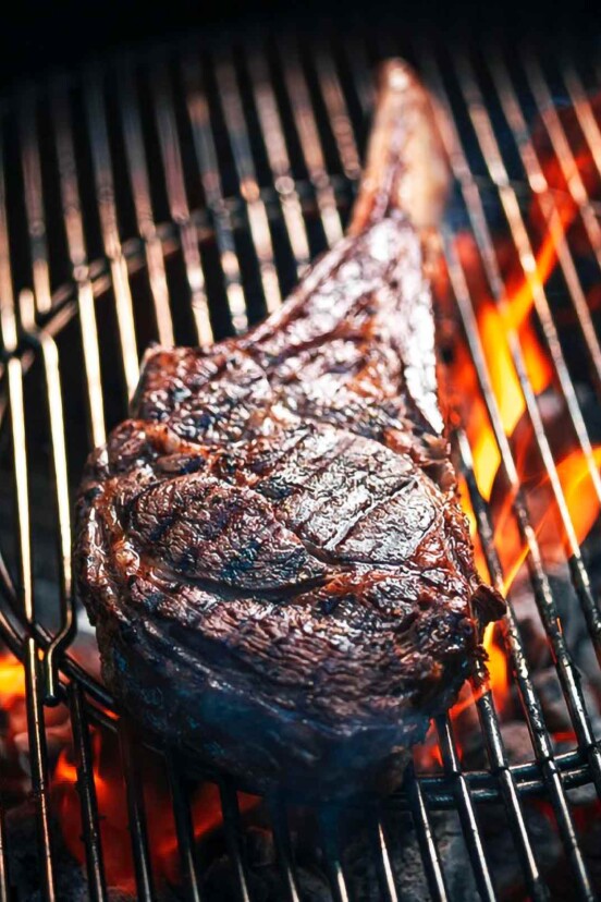 A grilled rib eye steak on a grill over open flame.