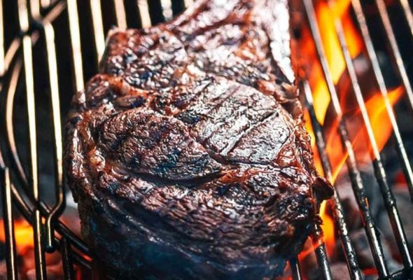 A grilled rib eye steak on a grill over open flame.
