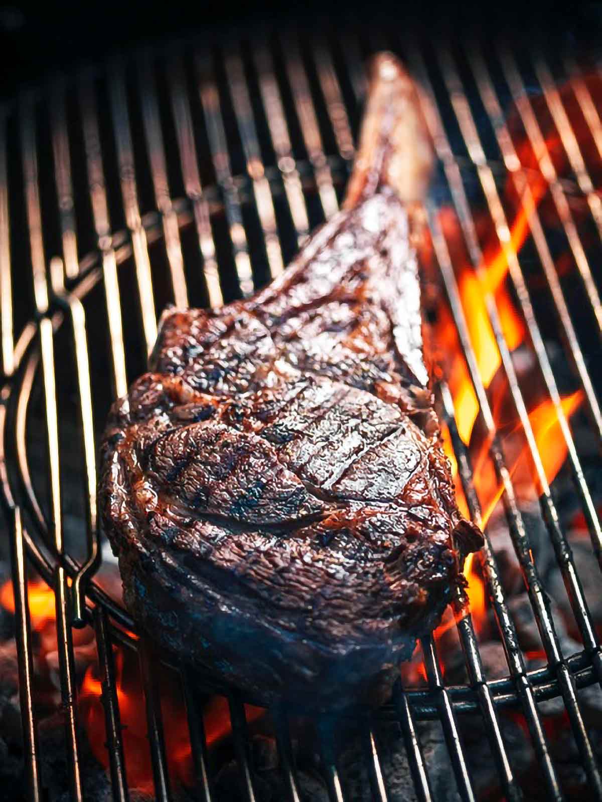 A grilled rib eye steak on a grill over open flame.