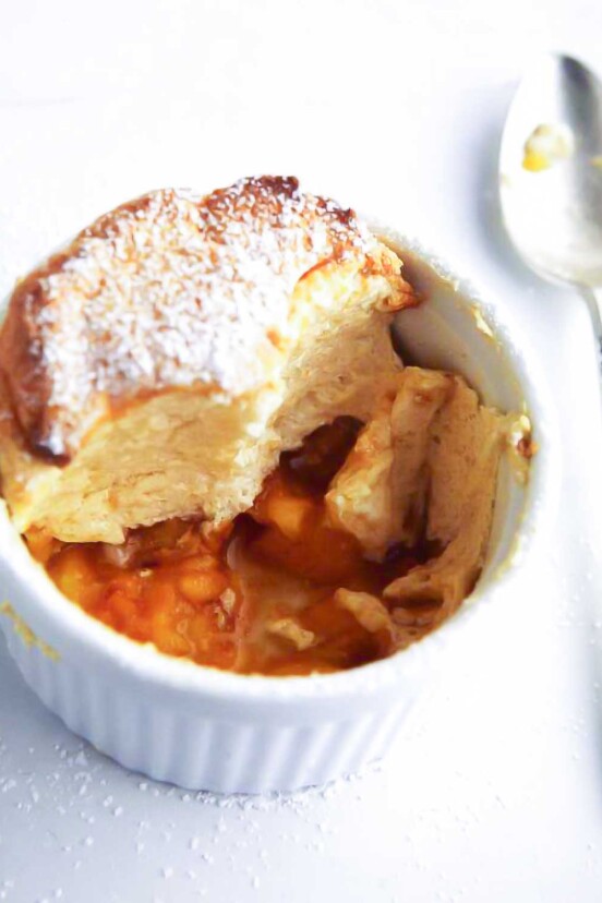 White dish of a sugar-dusted individual peach souffle; in the bottom are peach slices