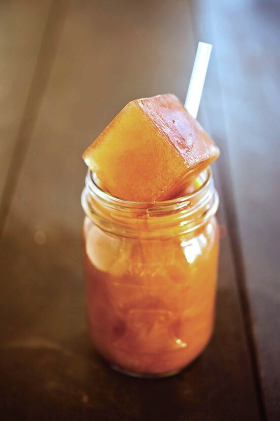 A mason jar filled with iced coffee, a straw, and a leftover coffee ice cube sticking out the top.