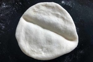 A round of papo-secos dough with a crease in the center.